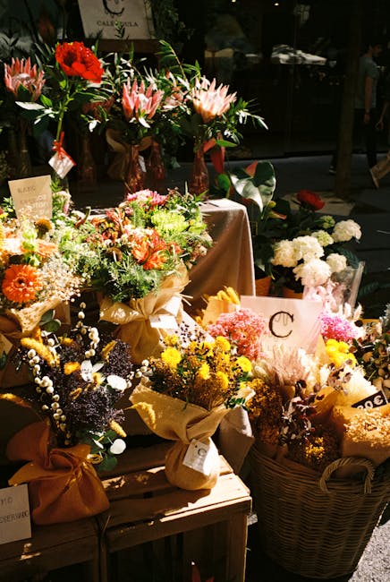 An assortment of fresh flower bouquets displayed outdoors at dusk, featuring vibrant arrangements of roses, lilies, gerbera daisies, and baby's breath in various colours such as red, pink, yellow, ora