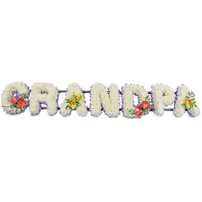 Set against a clean, uncluttered white background, a bespoke funeral tribute spells GRANDPA in large, block capital letters, similar to those often chosen by families in Silvertown to honour a beloved grandfather. Each letter is formed from compact clusters of snowy white chrysanthemums, positioned so closely that their petals interlock, creating a plush, textured surface reminiscent of a soft quilt. The whiteness is serene and understated, radiating a sense of peace and reflection. Along the base of each letter, a band of light lavender ribbon offers a delicate, pastel outline; its cool tone gently frames the letters and subtly lifts them from the background. Dark green structural bars run quietly behind, connecting and supporting the shape of the name. Colourful floral sprays are woven thoughtfully into the tribute. On the G and the D, rich red anthuriums, with their glossy, heart-shaped spathes and bold yellow spadices, are nestled into clusters of dark green foliage and tiny purple filler flowers, adding depth and an expression of heartfelt affection. The first and last A feature clusters of yellow-green orchids, their elegant petals and intricate throats showcased against fresh greenery, bringing a touch of modern refinement that feels at home in the evolving landscape around Silvertown Quays. The flowers look freshly cut and carefully placed, suggesting expert local craftsmanship and same-day preparation for a service at a nearby church, crematorium, or dockside farewell. Overall, the design is both strong and tender, offering a personalised, visually striking way for loved ones to pay their respects and remember Grandpa with grace.