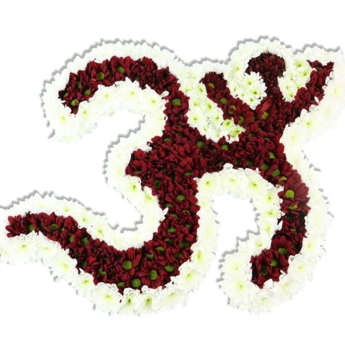 Rendered with patient artistry, this floral Om (Aum) arrangement presents the sacred Sanskrit sign as a living mosaic of tiny blooms against a spotless white background. The bulk of the symbol is a rich field of dark red or maroon chrysanthemums-small, pompon-like heads packed so closely the surface reads as velvety and continuous-each revealing a modest lime-green centre that adds delicate punctuations of colour. The emblem's signature '3' curve, the extended curved stroke descending from the base, and the upper crescent-with-dot are all meticulously modelled from these dense red clusters. Surrounding and accenting the interior curves is a thick, scalloped border of pristine white spray chrysanthemums, their fine textures and pointed petals lending a crisp contour that elevates the motif's readability and spiritual presence. The arrangement sits with a soft drop shadow that suggests gentle elevation and dimensionality; the petals themselves appear cool to the touch and slightly silky, layered in such a way that light pools and creates soft highlights along the ridges. A subtle, grounding fragrance-earthy with a hint of green-emerges from the maroon blooms, making the piece appropriate for contemplative ceremonies, yoga and meditation gatherings, or respectful memorial displays. Local context anchors the design: this is the kind of floral tribute you might see carried from Silvertown's quayside spaces toward Canning Town or placed near the Thames Path by Royal Victoria Dock during cultural observances, where craftsmanship and local devotion meet in a quiet, contemplative aesthetic.