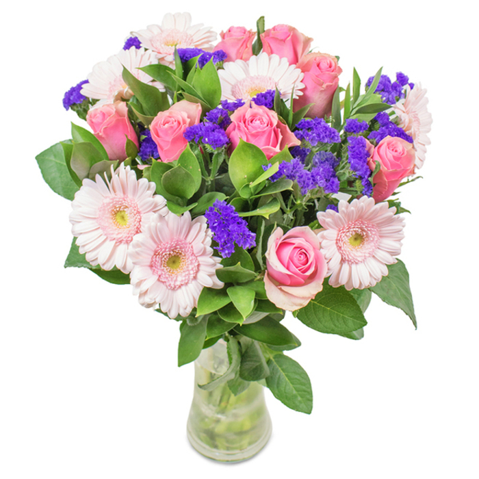 In this distinctive arrangement from Flower Delivery Silvertown, approximately 7-9 medium pink roses with elegantly swirling petals, just opening or still tightly nestled, take centre stage. These are complemented by around 5-7 pale pink gerbera daisies, recognisable for their large, open faces and soft, almost luminescent centres. Clusters of vivid purple statice provide textural contrast and an energetic splash of colour, reminiscent of Silvertown's vibrant weekend markets. A lush cascade of deep green foliage anchors the entire display, its freshness apparent in every glossy leaf-a subtle homage to the nearby green corridors along the Thames. Arranged in a clear, modern glass vase, the bouquet's stems rest in crisp water, suggesting a just-delivered freshness ideal for homes, offices, or special events across the Silvertown area. Set against a clean white background, this bouquet harmoniously blends contemporary flair and timeless sentiment, perfect for birthdays, anniversaries, or expressions of gratitude. Every bloom is thoughtfully placed, allowing the natural charm of Silvertown to shine through, creating a floral feature that evokes warmth, celebration, and local pride.